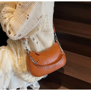 Detail of orange faux crocodile baguette bag with chain strap on a wooden staircase