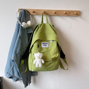 Close-up of light green nylon backpack with white logo patch and cute plush bear charm