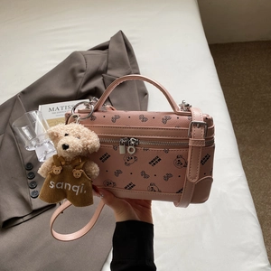 Detail view of pink leather crossbody bag with teddy bear pattern and plush charm accessory