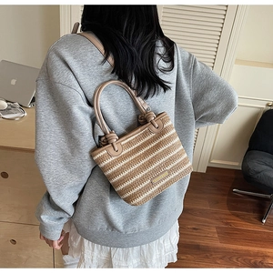 Detail of hand-woven straw tote with striped pattern and leather handles in a lifestyle setting