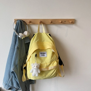 Detail of bright yellow backpack with white bear plush charm and logo label on front