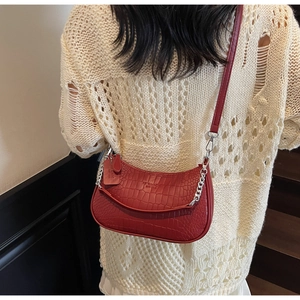 Close-up of red crocodile embossed baguette bag with silver chain and logo on white knit