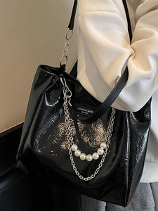 Black glossy tote bag with pearl chain detail worn by a model in casual white hoodie