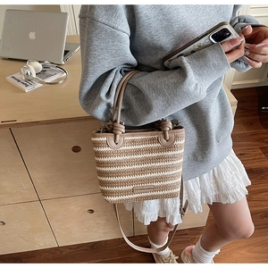 Detail of woven straw bucket bag with leather handles and metallic fashion plaque