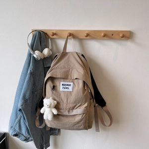 Detail view of khaki canvas backpack with minimalist letter patch and cute plush bear charm