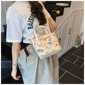Detailed close-up of a white bucket bag with colorful graffiti and gold metal hardware