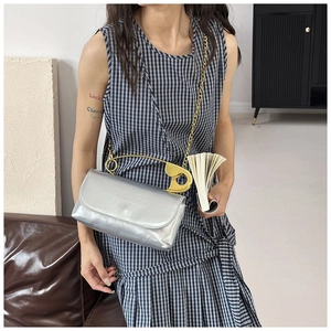 Détail d'un sac bandoulière argenté avec poignée épingle de sûreté dorée et chaîne