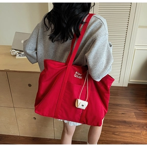Vue détaillée d'un grand sac cabas en nylon rouge avec lettrage blanc et une petite pochette