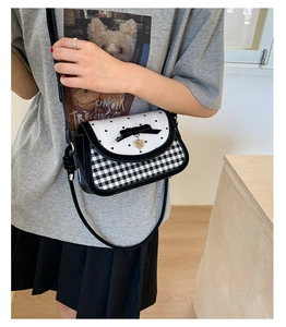 Close-up of heart charm, bow detail, and black-and-white checkered crossbody bag texture