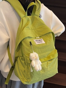 Minimalist bright green nylon backpack with plush bear charm on a model's back