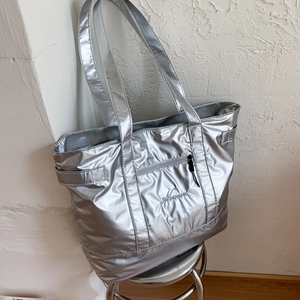 Detail of silver quilted tote bag with metallic finish and embroidery on a stool