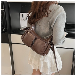 Detail of coffee brown glossy leather bag featuring multiple front zip pockets and shoulder strap