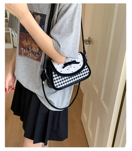 Detail of checkered crossbody bag with black bow and silver heart pendant decoration