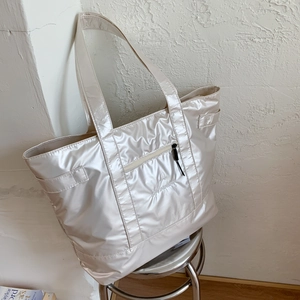 Detail of quilted silver nylon tote bag with embroidery on a metal stool