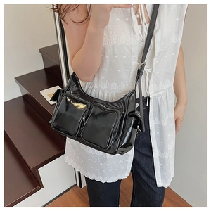 Detail view of glossy black Y2K shoulder bag with multiple zippers and pockets on stairs