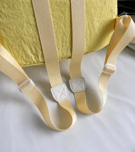 Detail of adjustable woven straps and stitching on a light yellow canvas backpack