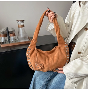 Détail d'un sac hobo en daim marron avec rivets argentés et breloque en forme de cœur