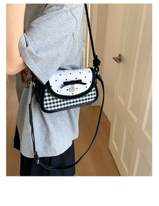 Detail of a black and white checkered crossbody bag with a bow and heart pendant