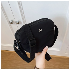 Close-up of the black nylon crossbody bag featuring double zippers and silver metal logo