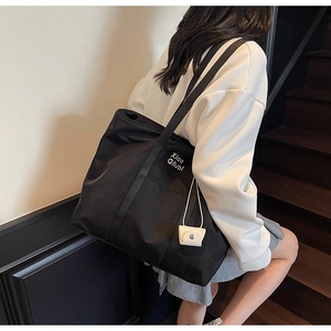 Vue latérale d'un grand cabas en nylon noir avec logo et charm porte-monnaie blanc assorti