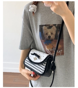 Detail of crossbody bag with black bow, heart pendant, and black-and-white grid pattern