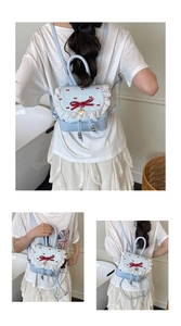 Detail view of light blue Lolita style backpack featuring white lace and red ribbon bows