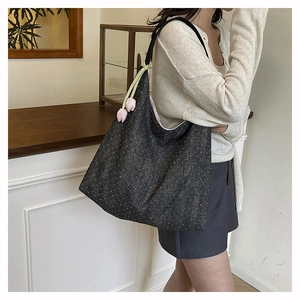 Detail of a black polka dot denim tote bag featuring a pink tulip flower charm accessory