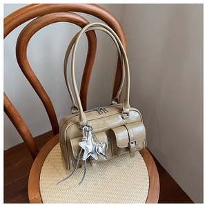 Détail du sac Boston beige avec poches extérieures à rabat et breloques étoile sur chaise en bois