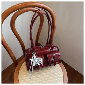 Détail du sac rouge foncé en cuir crocodile avec breloques argentées sur chaise