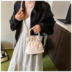Detail view of white drawstring bucket bag with purple beads and pleated texture