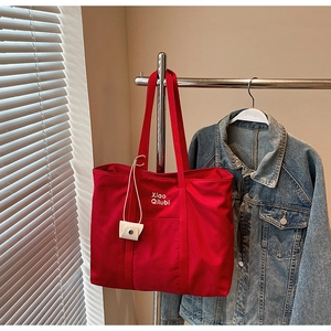 Détail du sac fourre-tout en toile rouge avec bretelles et logo blanc Xiao Qilubi