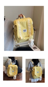 Detail of light yellow nylon backpack with flap closure and white plush bear keychain accessory