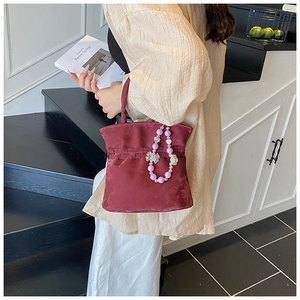 Detail of burgundy suede bucket bag with floral beaded charm against a modern staircase