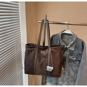 Détail du grand sac cabas café avec logo et breloque bleue sur une veste en jean