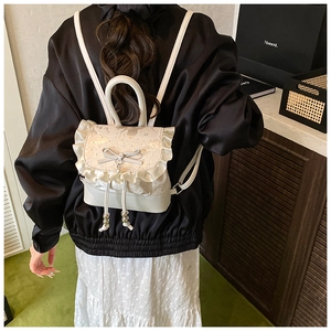 Detail view of a white mini backpack with elegant lace ruffles, bow, and pearl charms