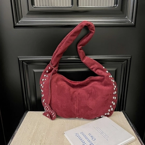 Détail du sac demi-lune en daim rouge foncé avec rivets argentés et pendentif cœur