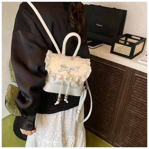 Detail of white mini backpack with lace ruffles, bow knot, and pearl pendant