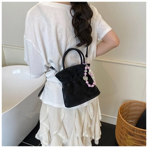 Detail of black velvet bucket bag with pearl bear charm and woven pleated edge