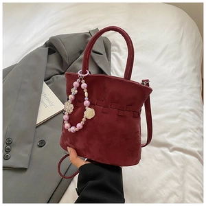 Detail view of burgundy pleated bucket bag with pearl floral charm on a grey blazer