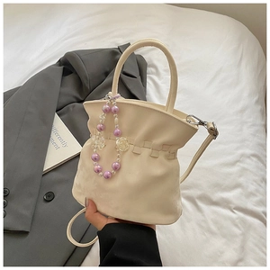 Detailed view of cream pleated bucket bag with decorative pearl and flower charm