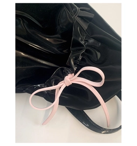 Close-up of black glossy tote bag featuring ruffled edges and a soft pink bow detail