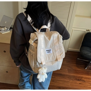 Detail view of beige nylon backpack with double straps and a cute white bear pendant