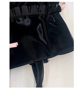 Close-up of glossy patent leather tote with pink bow detail and pleated ruffle edges