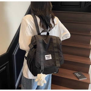 Detail of black nylon backpack with waswac rules label and cute white plush bear pendant