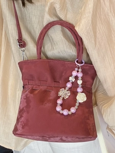 Deep red pleated bucket bag with decorative pearl charm and adjustable shoulder strap