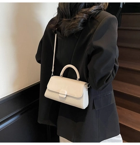 Detail of beige crossbody bag with woven leather texture worn over a black blazer