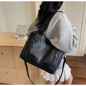 Close-up of black pebble leather tote bag featuring dual vertical silver zipper pockets