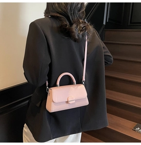 Pink crossbody bag with textured leather shown being worn on a warm indoor staircase