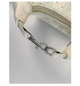 Macro detail of cream shoulder bag showing silver lobster clasp and sequin fabric texture