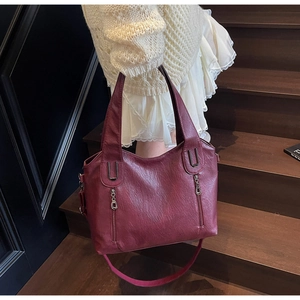 Detail of burgundy lychee leather tote bag with vertical zippers on a wooden staircase